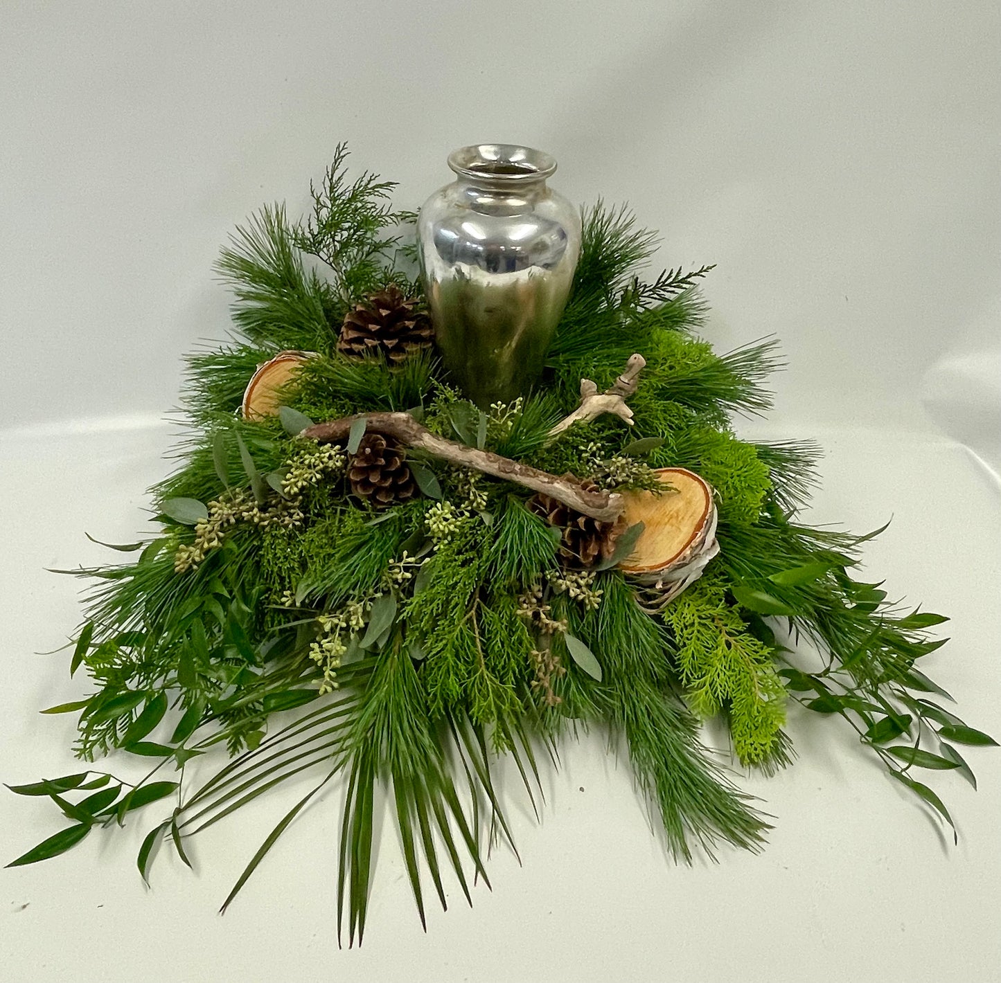 Composition naturelle entourant une urne en métal, composée de branches de bouleau, de cocottes, de morceaux de bois et de feuillages des bois, évoquant la sérénité et la tranquillité de la nature.