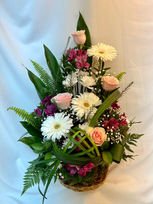 Arrangement floral “Bruine de bonheur” dans un panier en rotin, comprenant des roses roses douces, des gerberas blancs éclatants, des alstroémères violettes et un beau feuillage, créant une ambiance de bonheur et de sérénité.