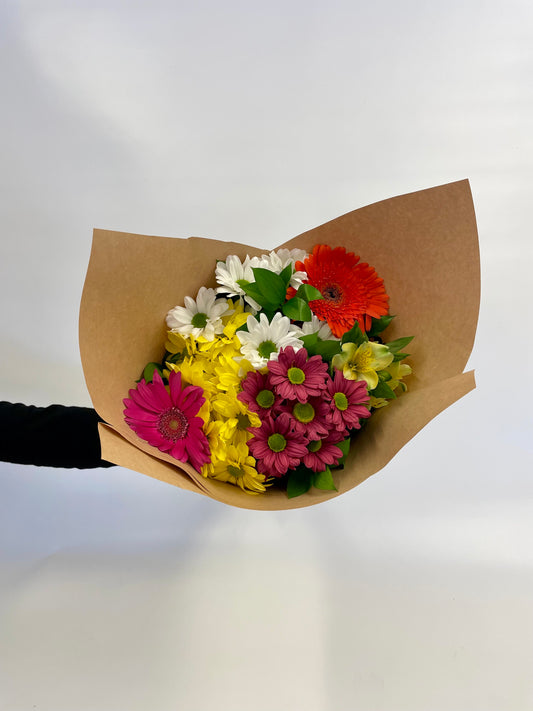 Bouquet de fleurs colorées composé de gerberas, de marguerites et d’alstroemères, présenté dans un papier kraft rustique, évoquant la beauté naturelle des champs fleuris.