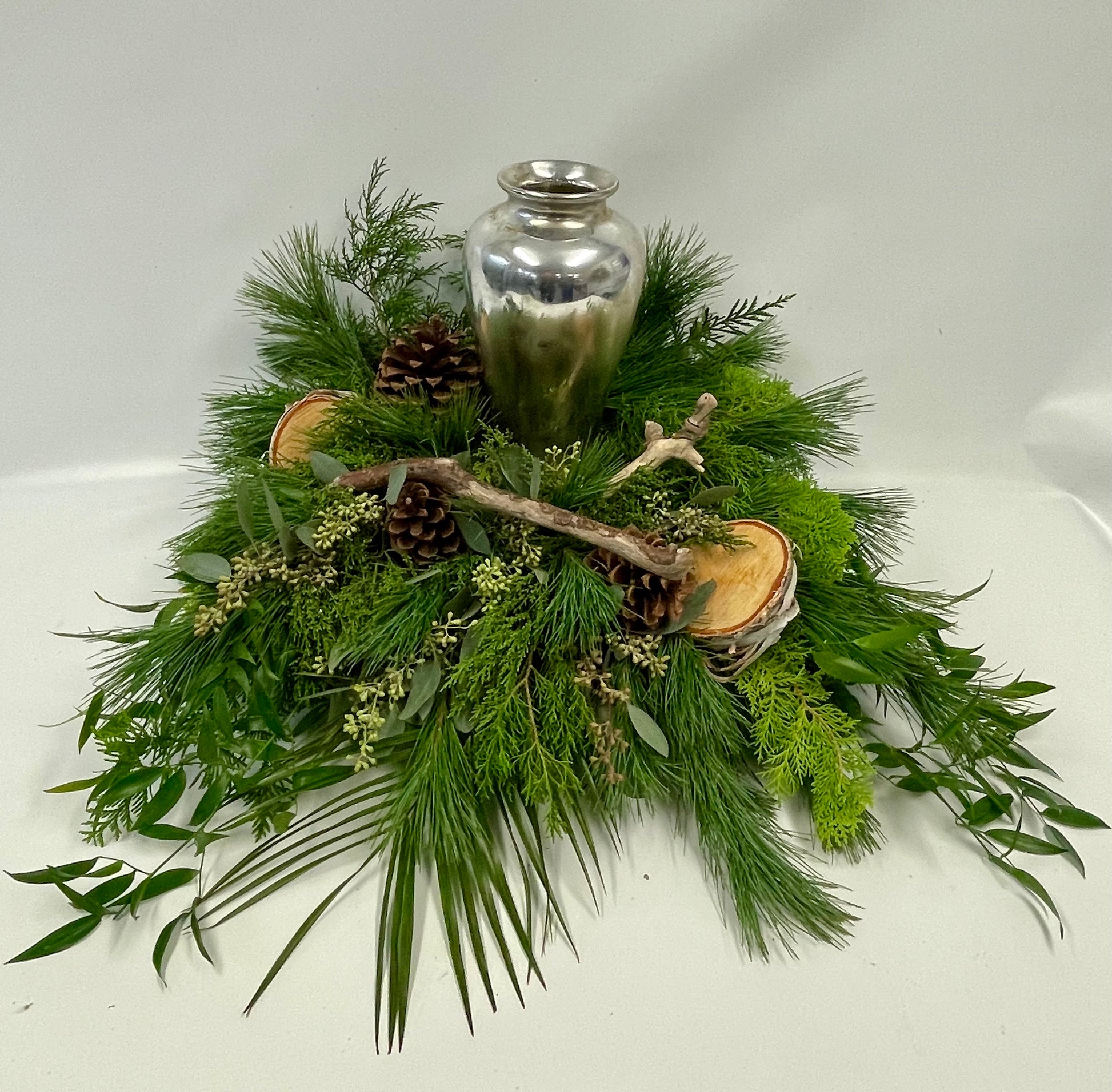 Composition naturelle entourant une urne en métal, composée de branches de bouleau, de cocottes, de morceaux de bois et de feuillages des bois, évoquant la sérénité et la tranquillité de la nature.