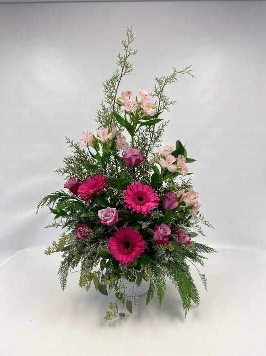 L’arrangement floral ‘Tendre Amie’ est une corbeille florale monochrome composée de gerberas roses vifs, de roses mauves délicates, et d’alstroémères roses pâles, enrichie de feuillages variés, offrant une harmonie parfaite de couleurs et de tendresse.